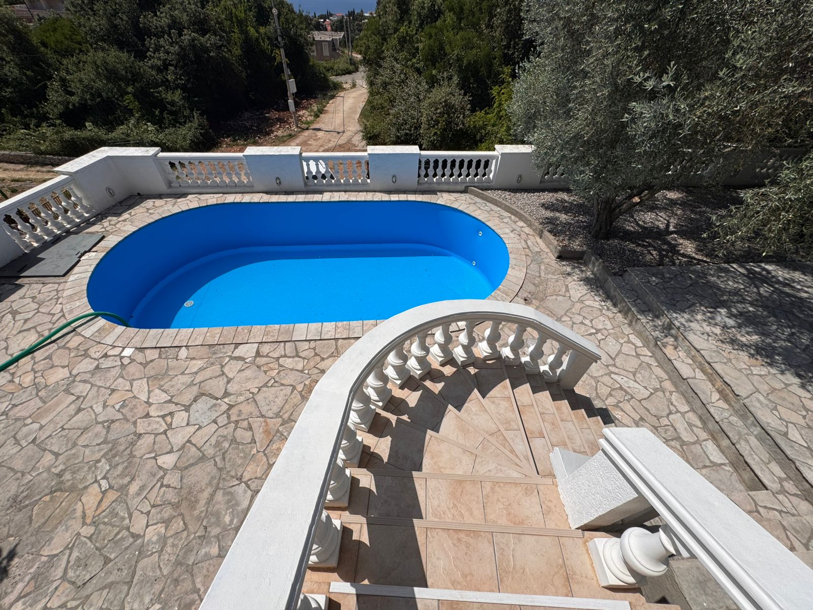 Elegant curved stone staircase with white railings to private pool, stone patio, and lush trees&mdash;prime Ulcinj real estate by ekosphere doo.