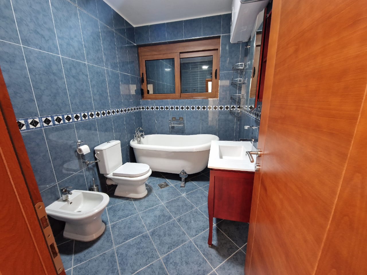 Modern bathroom in Ulcinj with blue tiles, freestanding tub, bidet, and window. Top Montenegro property by Ekosphere on immobilien.ekosphere.me.