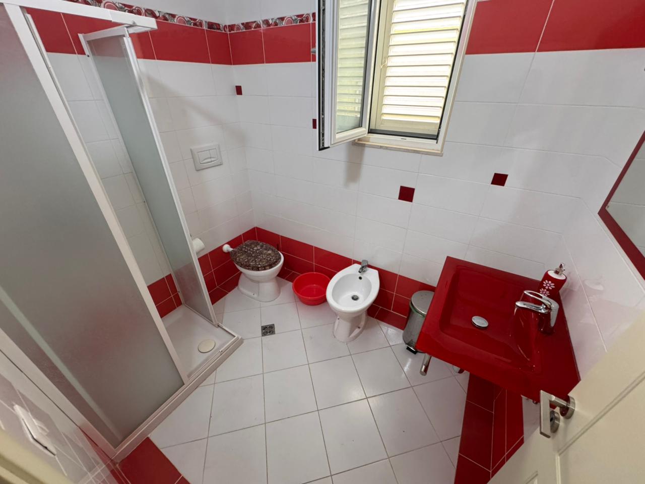 Modern bathroom in Ulcinj property: white/red tiles, shower, bidet, red sink. Invest via immobilien.ekosphere.me by ekosphere doo.