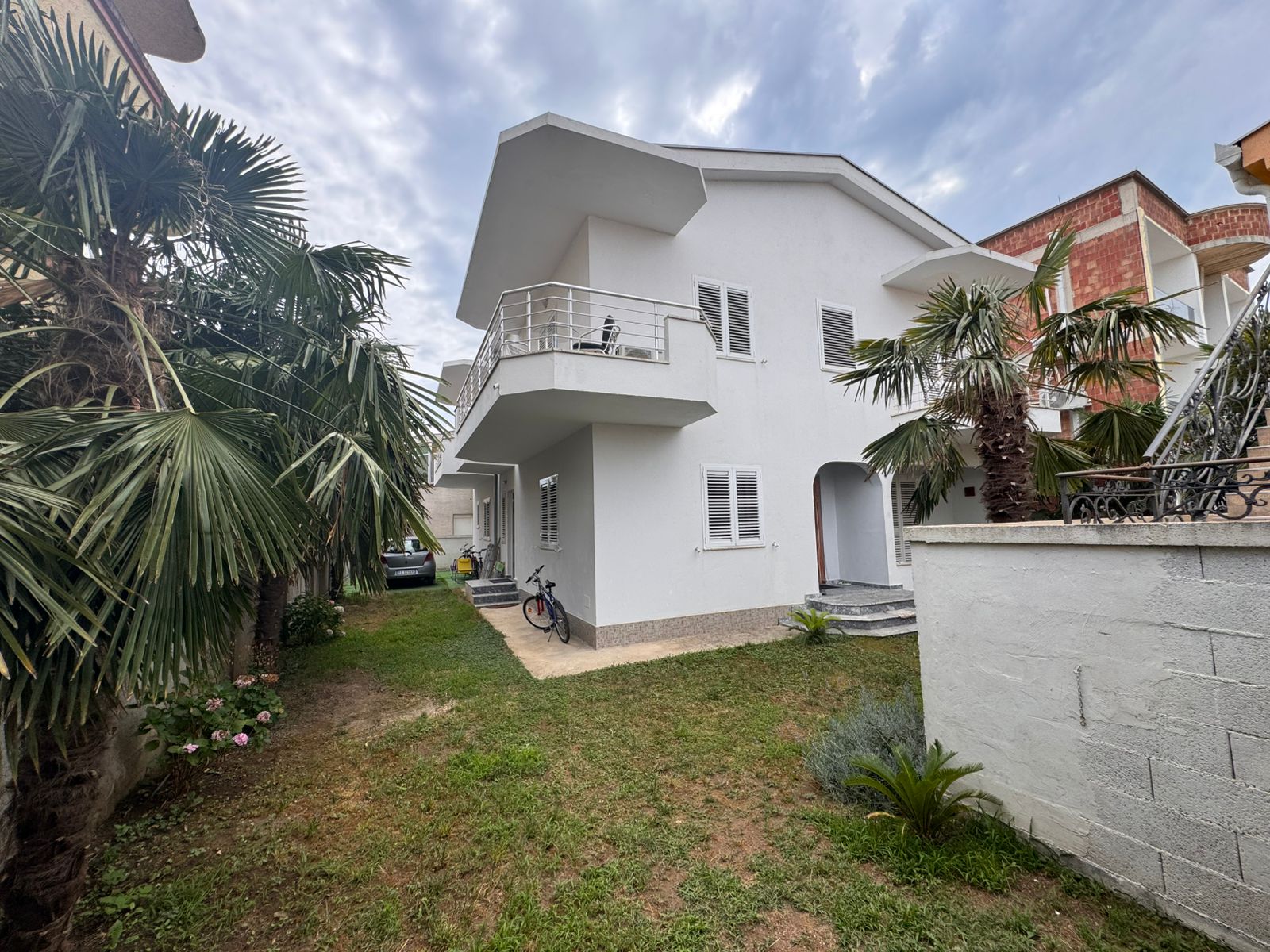 Elegant two-story white home in Ulcinj, Montenegro with balcony, palms, car and bike&mdash;prime real estate. Listed by ekosphere doo.