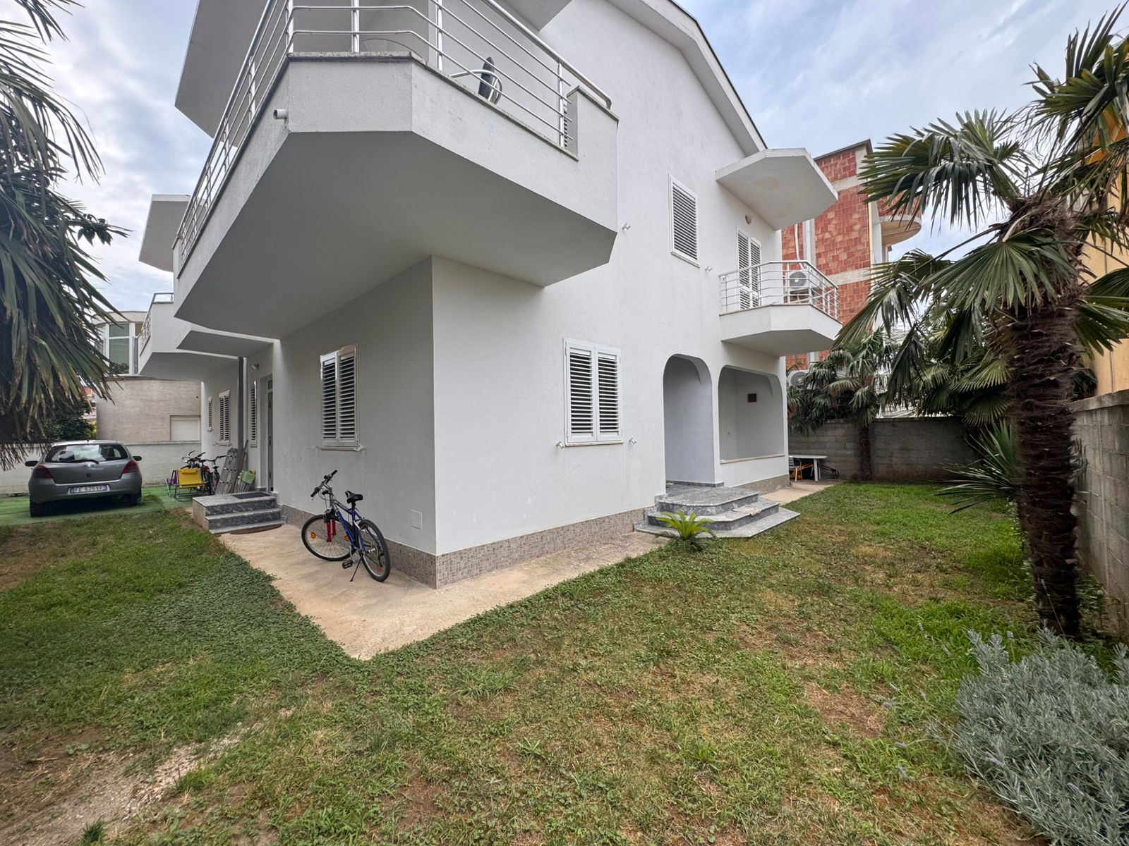 Modern white two-story house in Ulcinj, Montenegro: balconies, eco-friendly yard, palm trees. Listed by Ekosphere doo on immobilien.ekosphere.me.