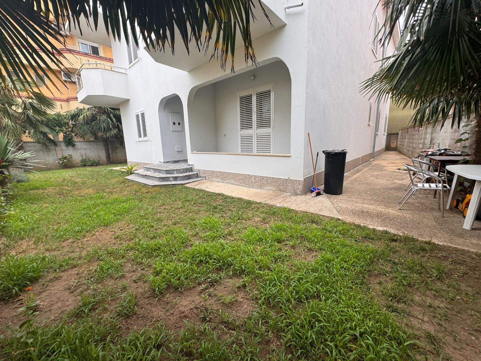 Modern white two-story home with porch, lush lawn, palm trees, and yard seating&mdash;prime Ulcinj real estate from Ekosphere on immobilien.ekosphere.me.
