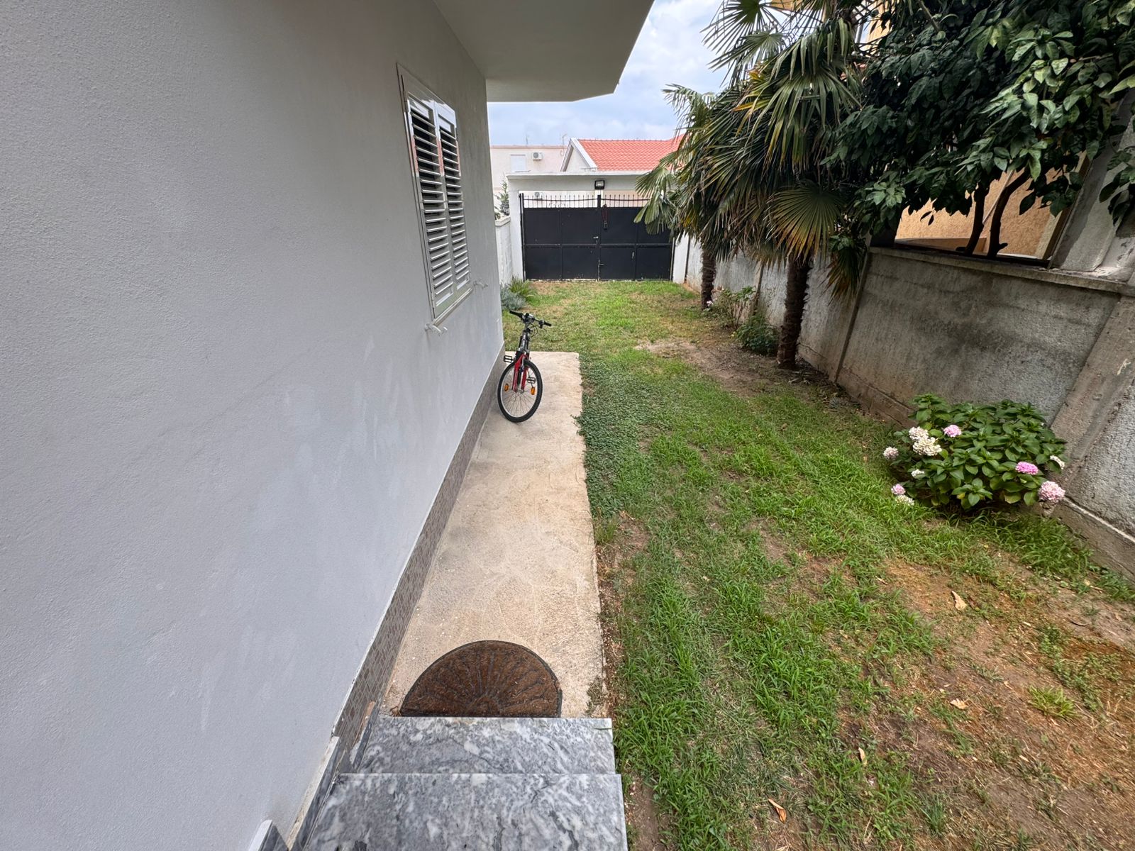 Modern Ulcinj property for sale&mdash;white house, lush plants, private path to secure gate. Invest via immobilien.ekosphere.me by ekosphere doo.
