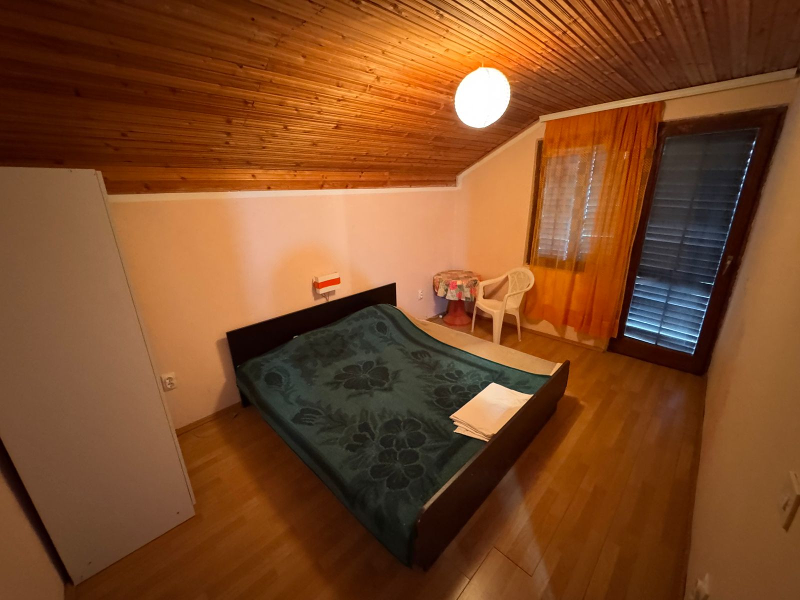 Inviting Ulcinj bedroom with sloped wood ceiling, double bed, orange curtains&mdash;ideal Montenegro investment. Listed on immobilien.ekosphere.me by Ekosphere doo.