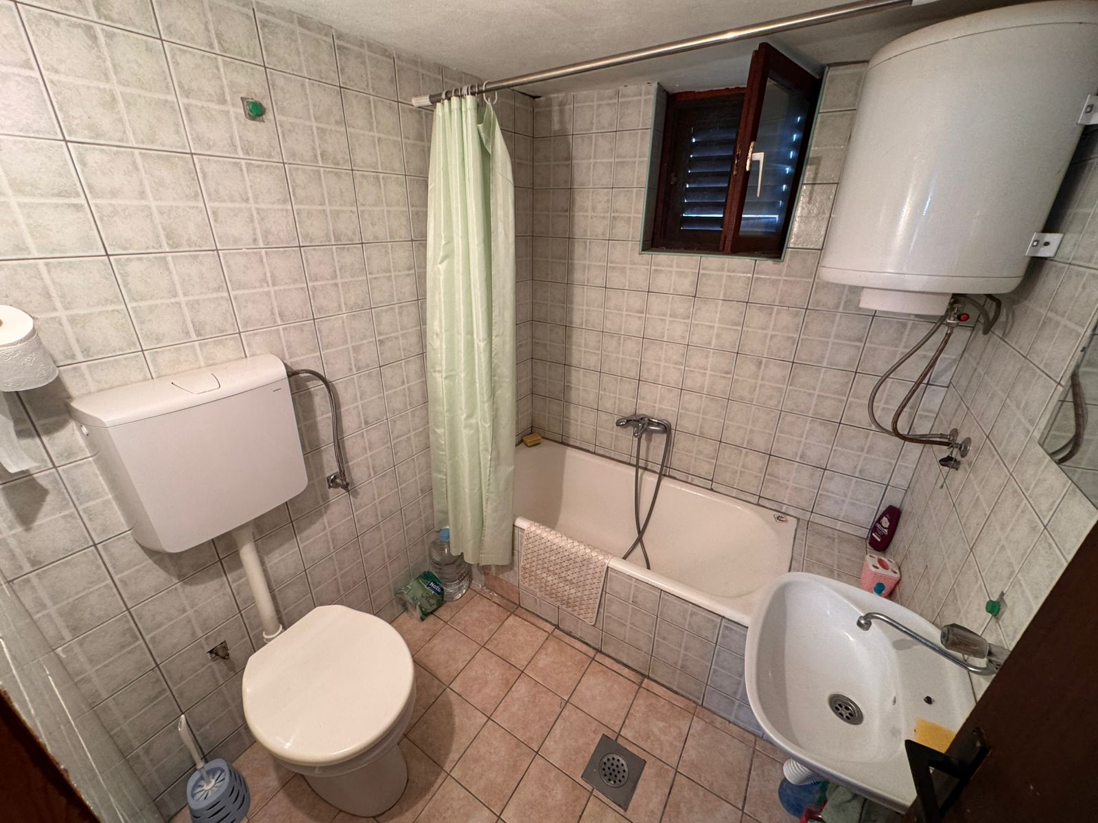 Modern tiled bathroom in Ulcinj property: toilet, eco water heater, tub with shower, sink, window&mdash;exclusive at immobilien.ekosphere.me.