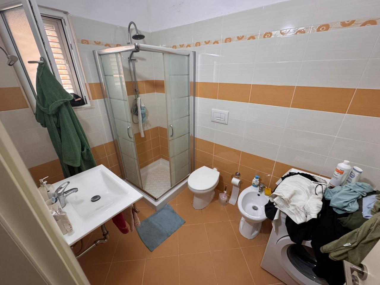 Modern bathroom in Ulcinj property with glass shower, bidet, washer, and orange tiles. Exclusive listing by ekosphere doo on immobilien.ekosphere.me.