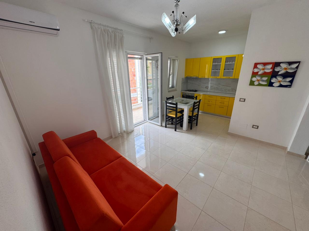 Modern Ulcinj apartment with red-orange sofa, yellow kitchen, and balcony. Prime investment via immobilien.ekosphere.me by ekosphere doo.