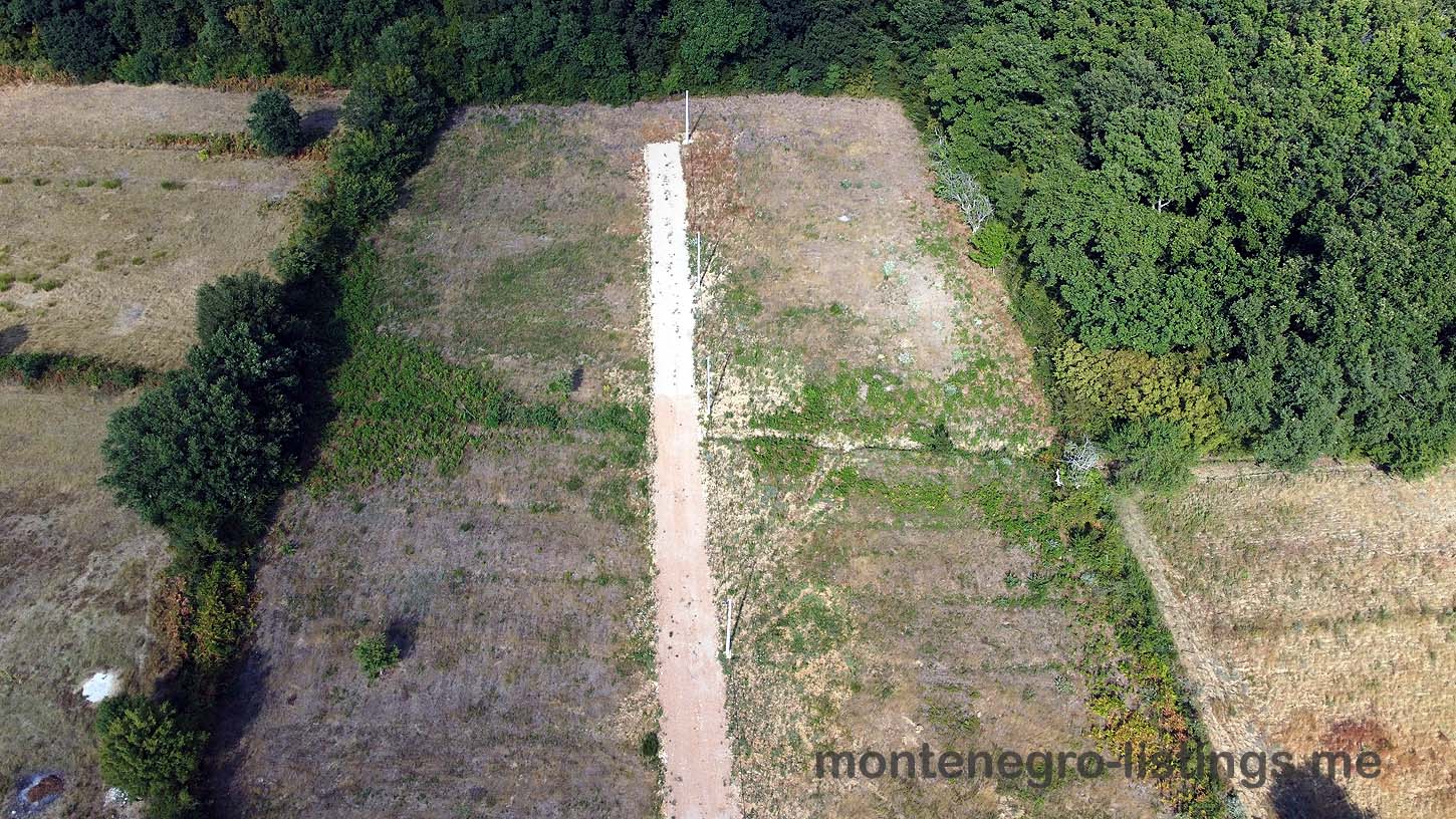 Aerial view of Ulcinj fields ideal for property investment, with road access and lush trees. Montenegro-listings.me by ekosphere doo.