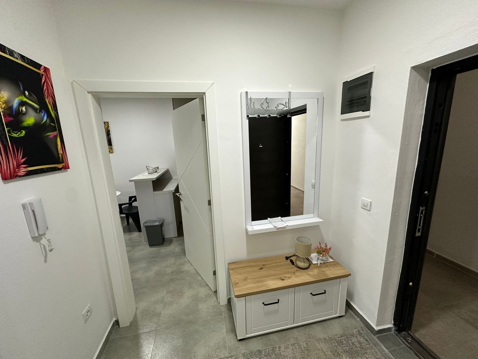 Modern hallway in Ulcinj property: gray tile floors, white walls, vanity, plant, and intercom. Montenegro-listings.me by Ekosphere.