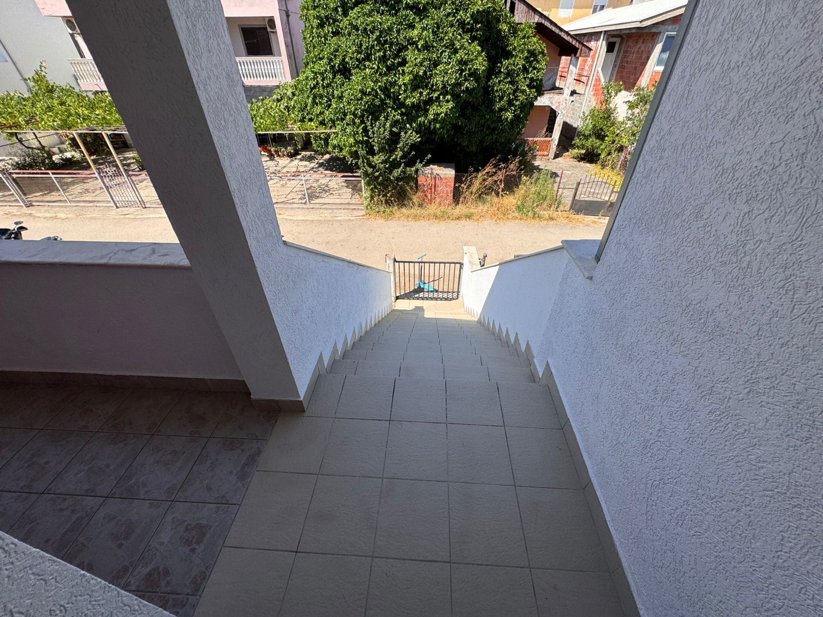 Stunning Ulcinj property: tiled stairs, secure gate, tree-lined street & white homes. A prime real estate investment via immobilien.ekosphere.me by ekosphere doo.