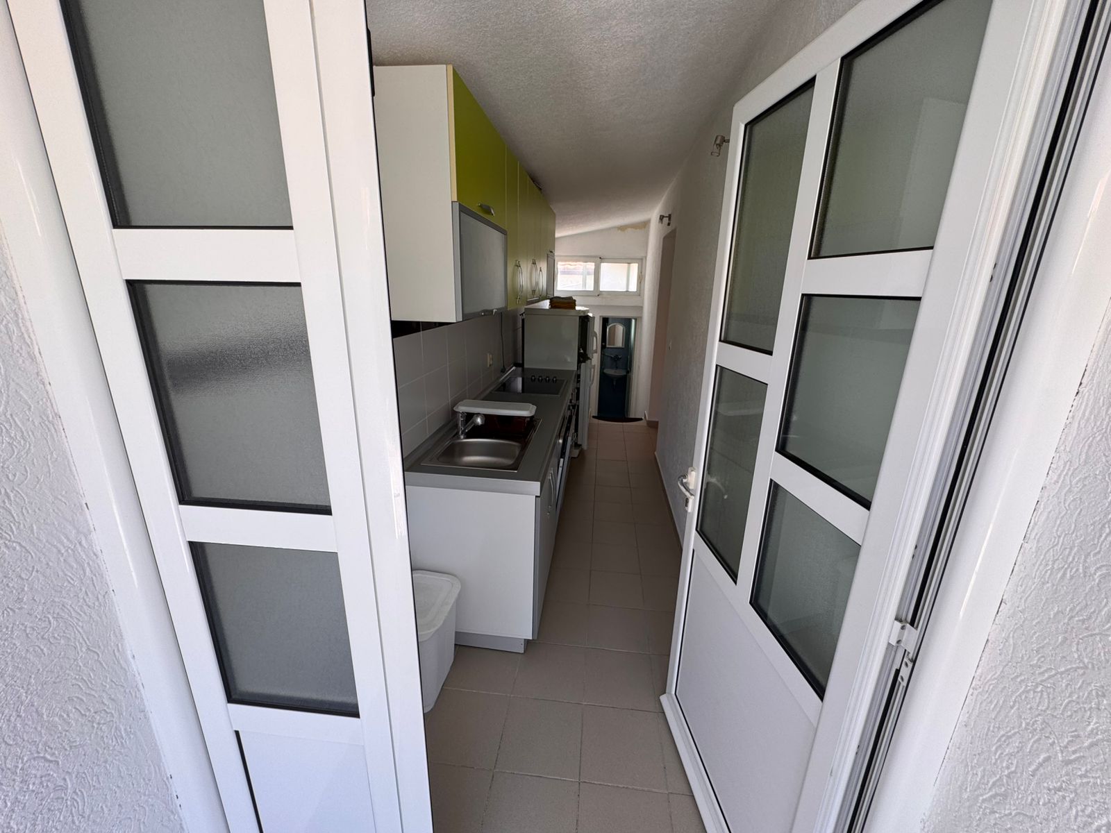 Modern narrow kitchen in Ulcinj property: sleek white cabinets, green accent, appliances, ideal Montenegro investment. By ekosphere doo.