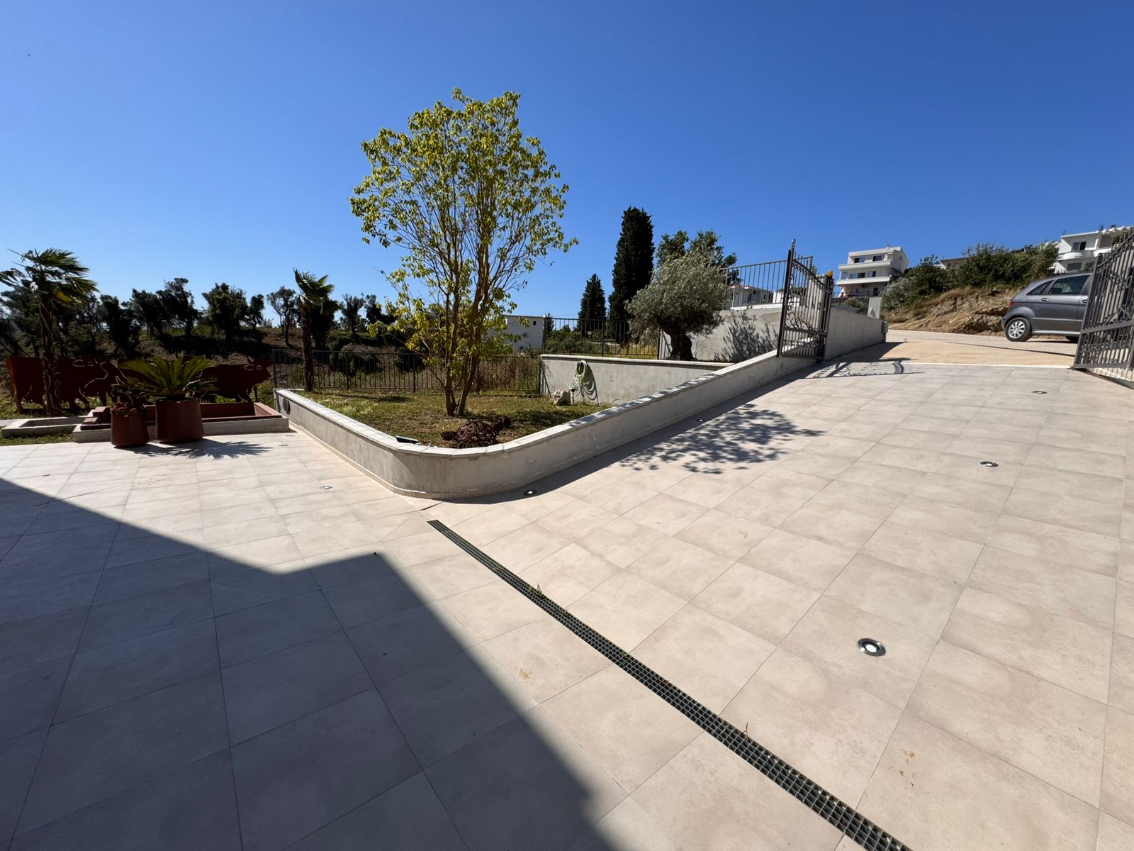 Modern paved terrace with elegant tiles, lush greenery, secure metal gate, and private parking&mdash;prime Ulcinj property on immobilien.ekosphere.me by ekosphere doo.