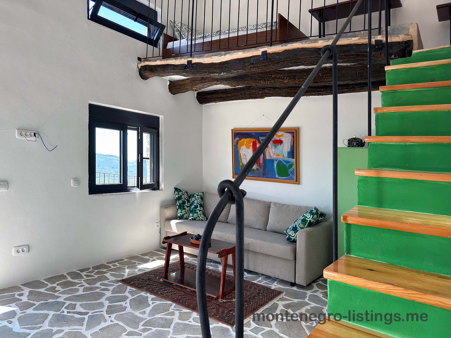 Ulcinj living room with gray sofa, vibrant cushions, wood table, green stairs. Exclusive Ekosphere property on immobilien.ekosphere.me.