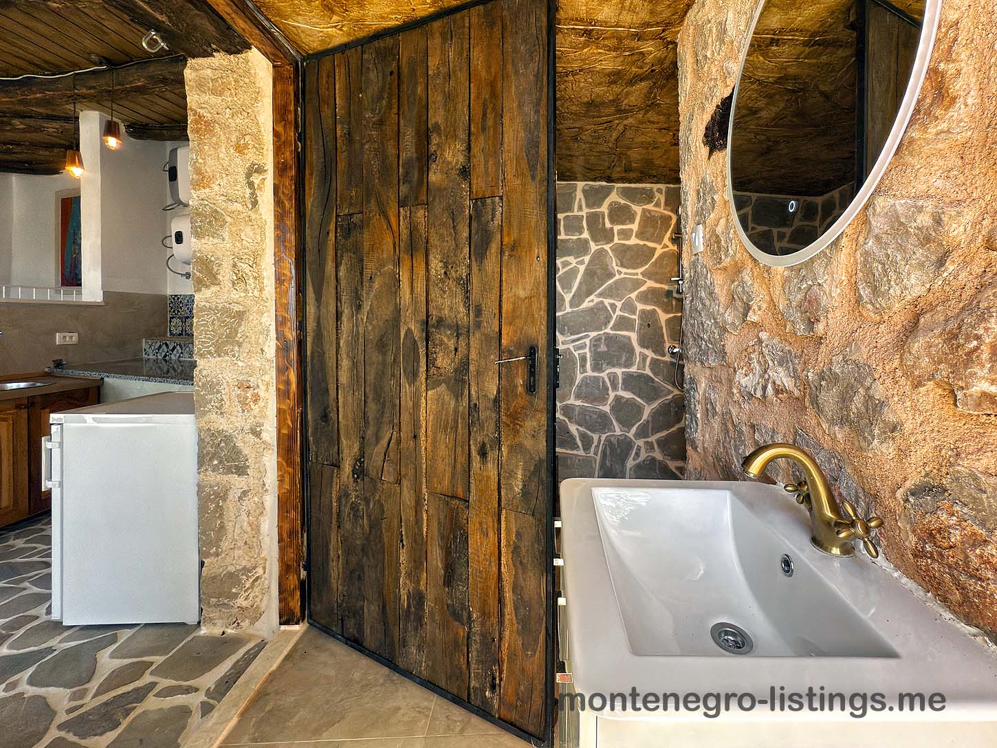 Elegant rustic bathroom with stone walls, wood door, chic brass accents; ideal Ulcinj investment via immobilien.ekosphere.me by ekosphere doo.