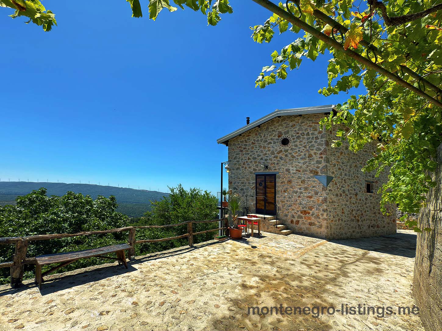 Stone house with wooden door, sunlit patio, greenery; top Ulcinj real estate by immobilien.ekosphere.me & ekosphere doo. Invest now!.
