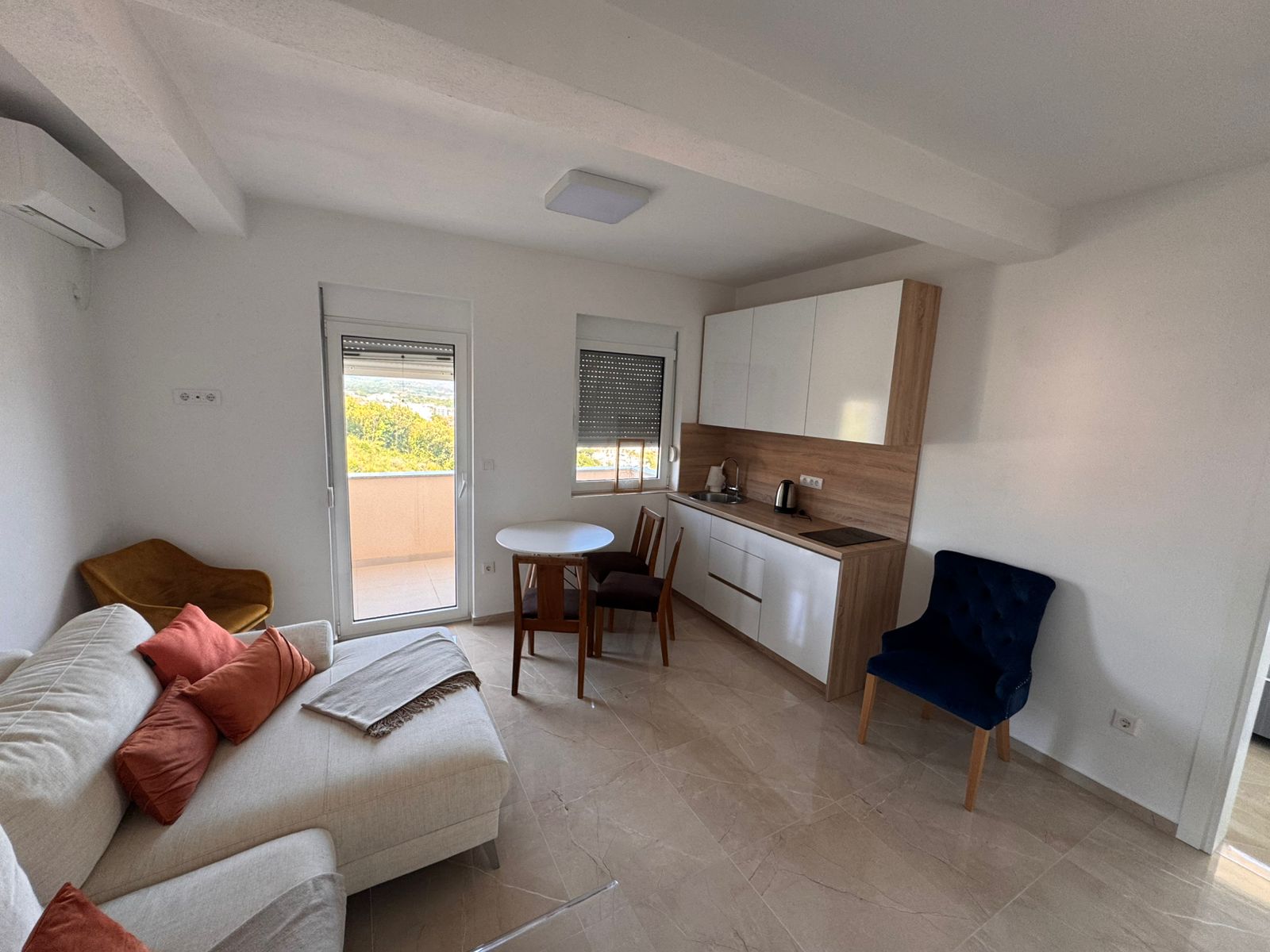 Modern Ulcinj apartment: white sofa, orange cushions, dining for two, balcony access. Top Montenegro investment at immobilien.ekosphere.me by Ekosphere doo.