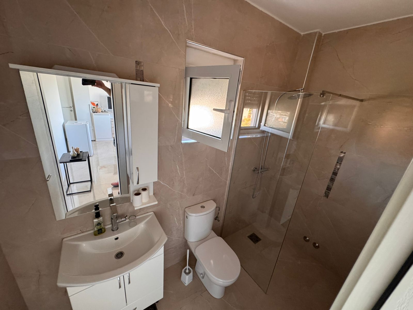 Contemporary Ulcinj bathroom: beige tiles, glass shower, window, and premium fixtures&mdash;ideal Montenegro real estate by ekosphere doo.