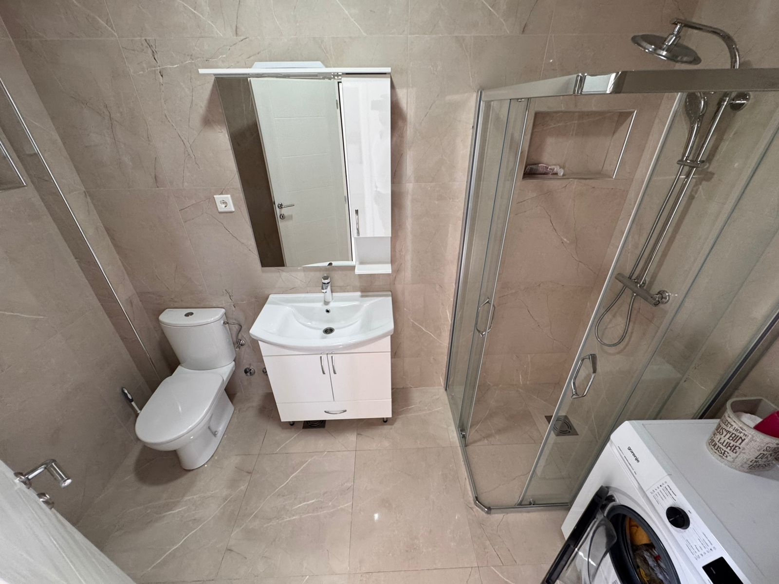 Contemporary bathroom in Ulcinj with beige tiles, glass shower, vanity, washer&mdash;ideal property investment listed at immobilien.ekosphere.me by ekosphere doo.