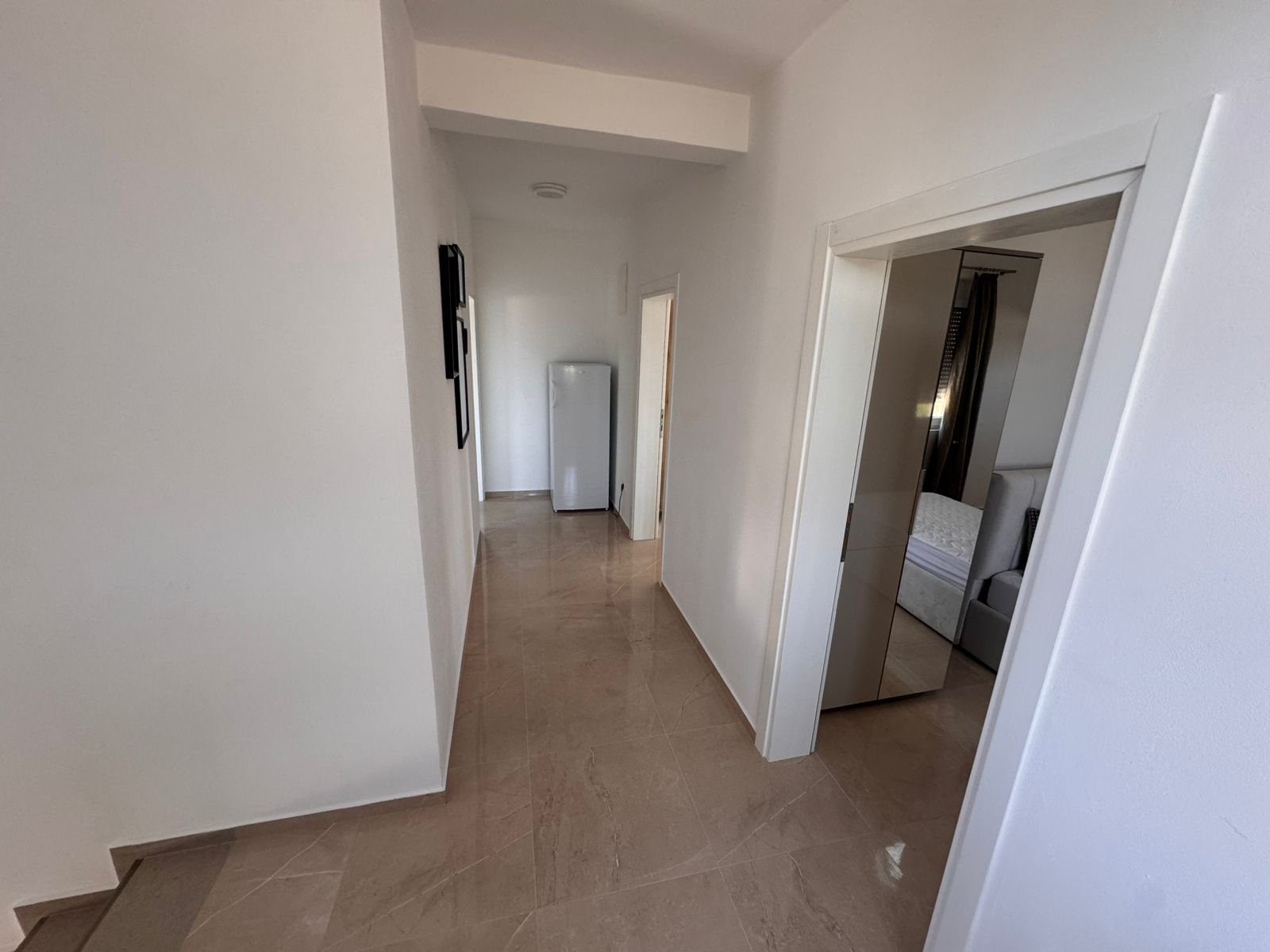 Bright hallway with beige tiles, white walls, and fridge leads to a bedroom&mdash;ideal Ulcinj investment. Listed by immobilien.ekosphere.me of ekosphere doo.