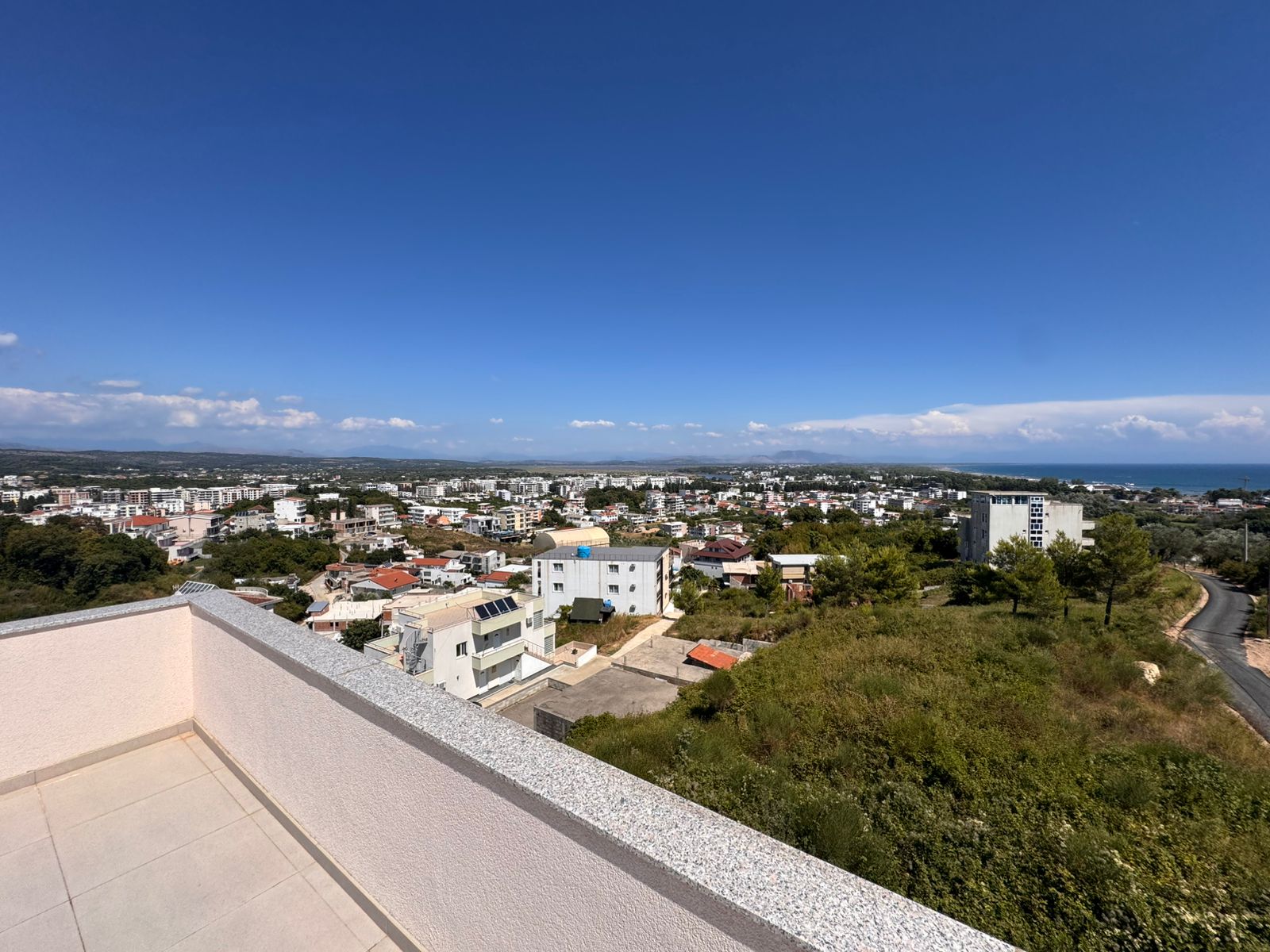 Stunning balcony view in Ulcinj, Montenegro: low-rise homes, lush greenery, sea horizon. Exclusive with immobilien.ekosphere.me by ekosphere doo.