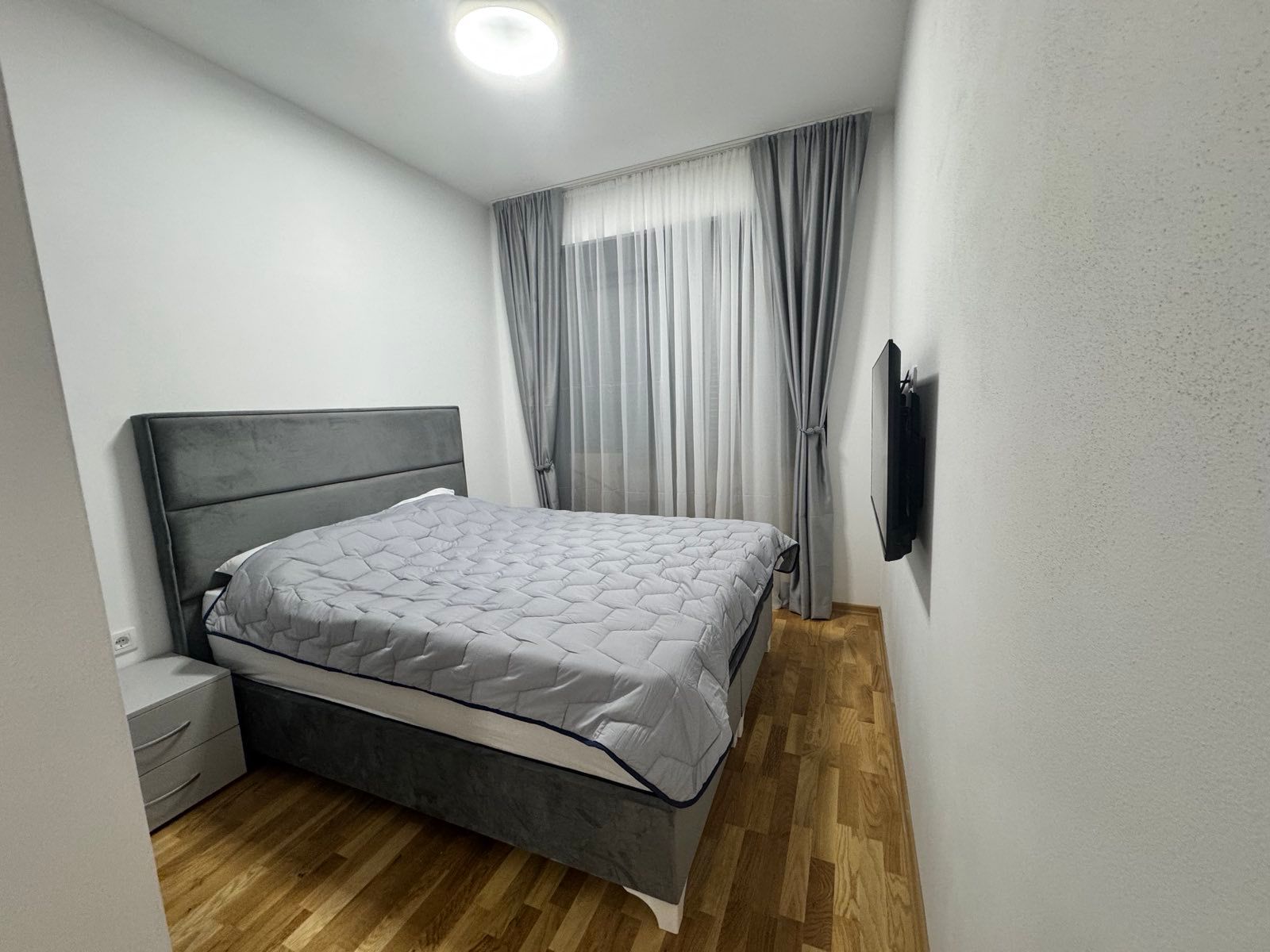 Elegant Ulcinj bedroom: spacious gray bed, wood floors, wall TV. Invest in Montenegro real estate at immobilien.ekosphere.me by ekosphere doo.