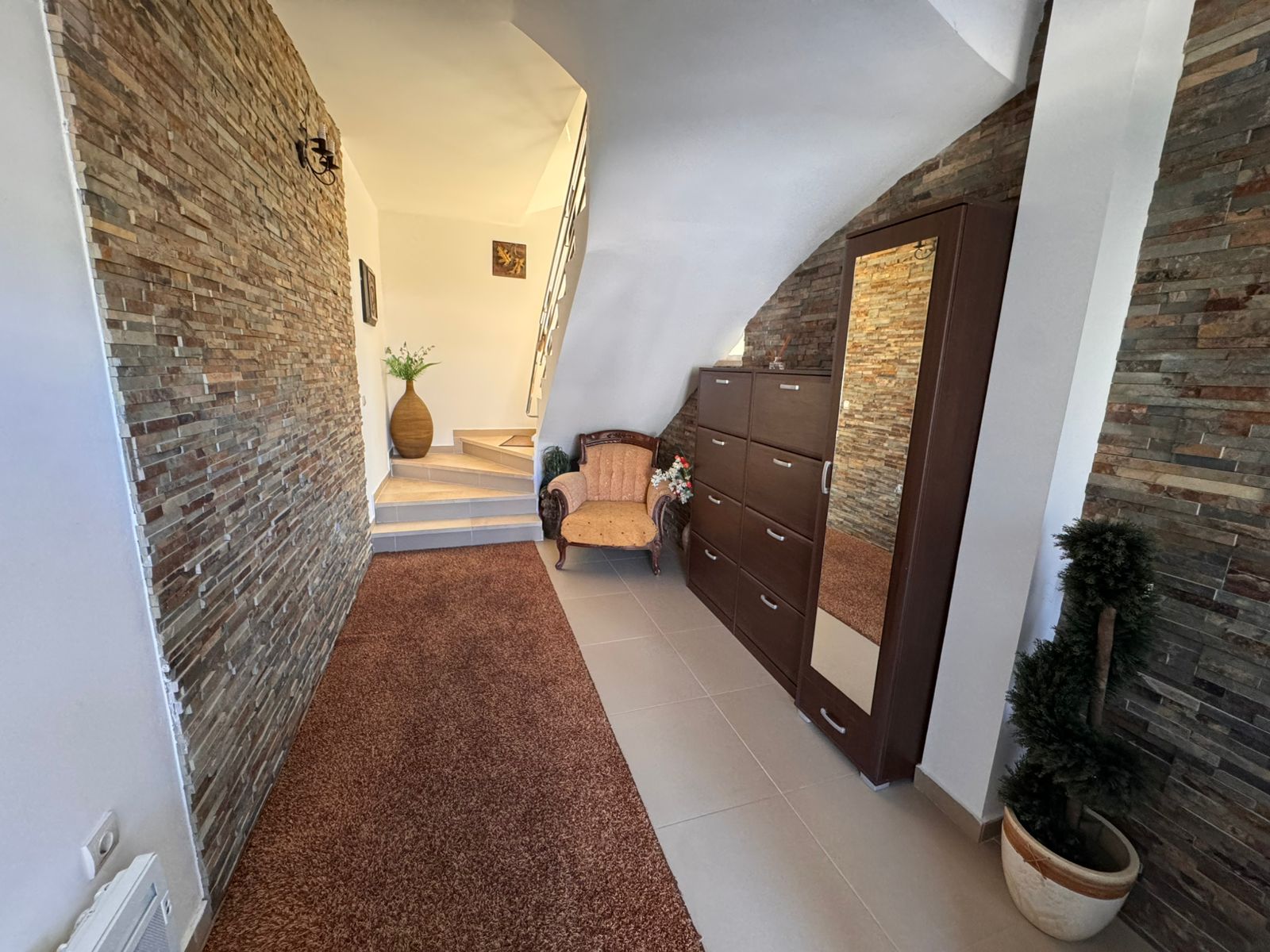 Elegant Ulcinj home with stone accents, plush chair, wood dresser, modern lighting; premium real estate on immobilien.ekosphere.me.