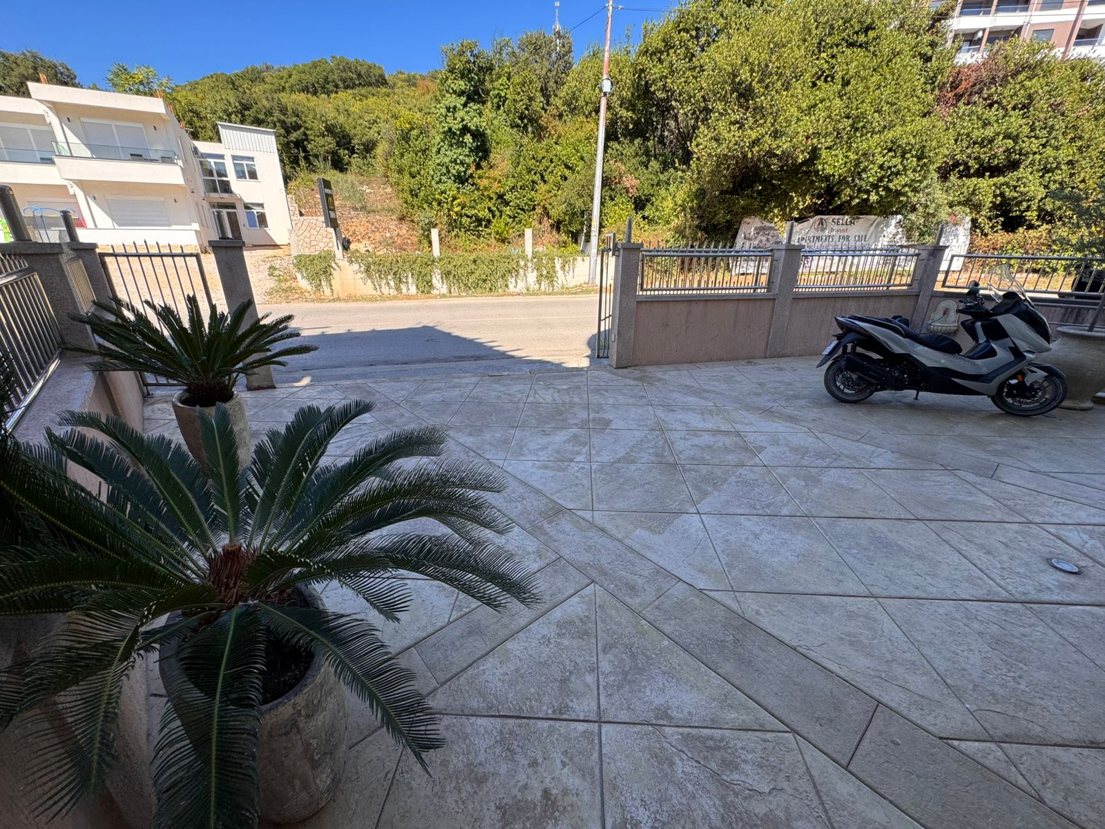 Modern tiled patio featuring lush potted greenery, secure metal fencing, and urban Ulcinj views&mdash;exclusive at immobilien.ekosphere.me by ekosphere doo.
