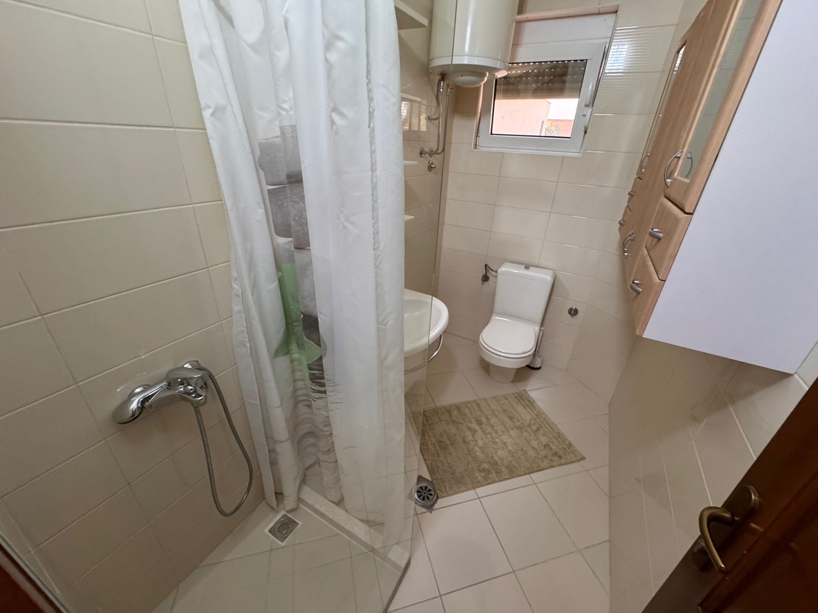 Modern bathroom in Ulcinj property: beige tiles, shower, window, cabinets; a top investment via immobilien.ekosphere.me by ekosphere doo.