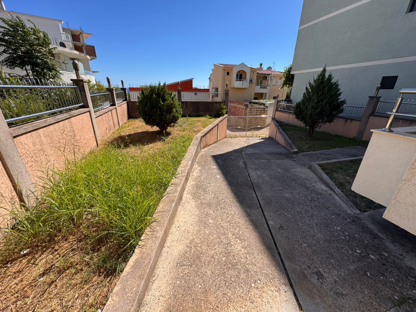 Inviting concrete driveway with lush grassy borders leads to secure gate, homes and apartments in scenic Ulcinj. Invest via Montenegro-Listings.me by ekosphere doo.