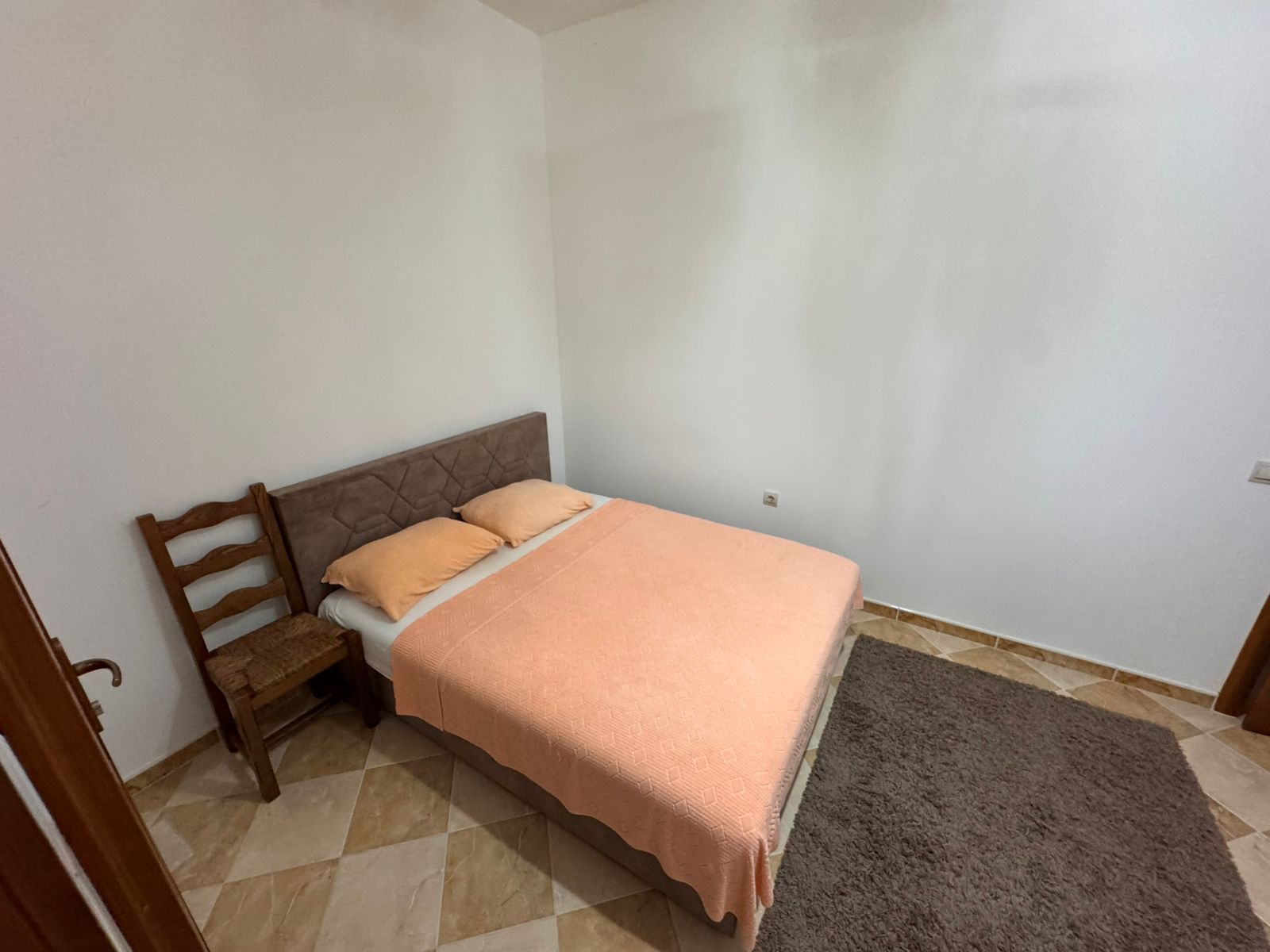 Modern Ulcinj bedroom with double bed, peach blanket, chair, tiled floor&mdash;ideal Montenegro investment. Exclusive on immobilien.ekosphere.me by ekosphere doo.