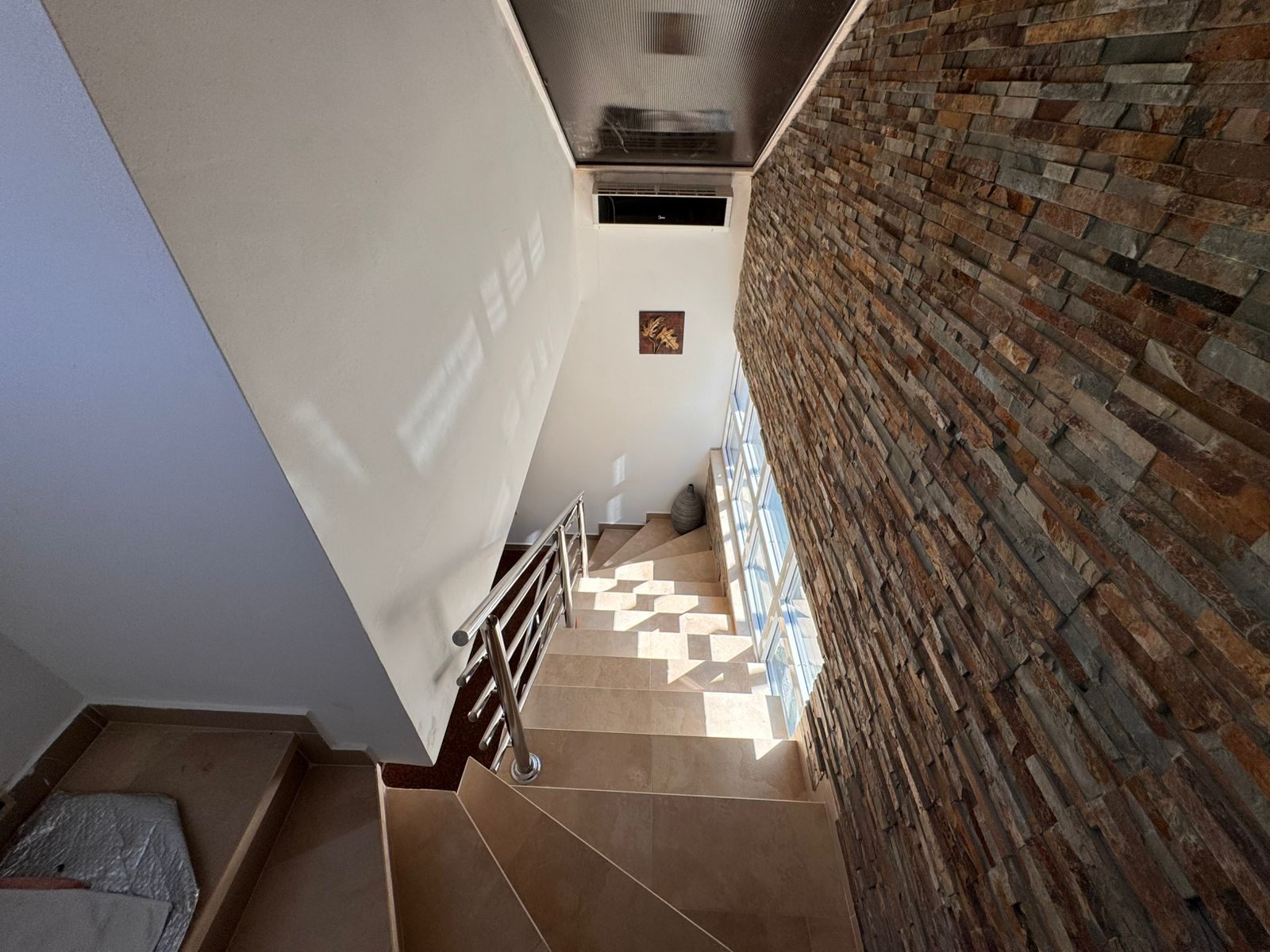 Elegant staircase with beige steps, metal railing, stone accents, and large windows&mdash;prime Ulcinj real estate on immobilien.ekosphere.me.