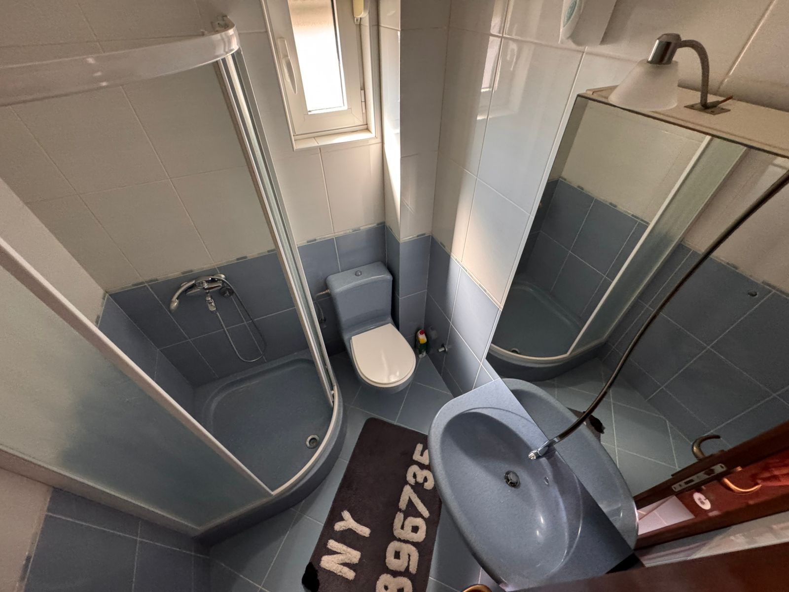 Modern bathroom in Ulcinj with blue tiles, glass shower, curved sink, and large mirror&mdash;exclusive real estate by ekosphere doo.