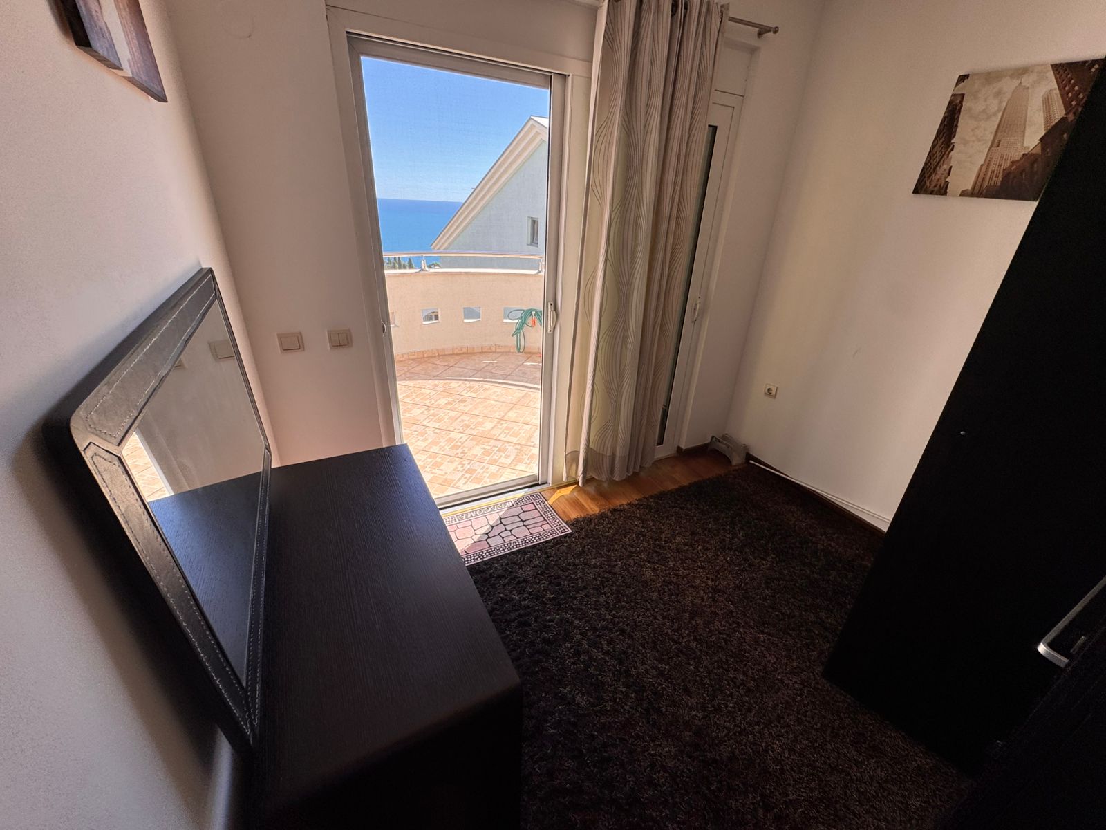 Modern Ulcinj apartment: stylish room with dark furnishings, sea-view balcony, glass door, and curated art. Exclusive on immobilien.ekosphere.me by ekosphere doo.