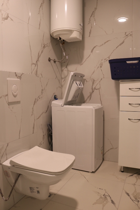 Modern Ulcinj bathroom with marble tiles, wall-mounted toilet, washer, water heater&mdash;investment opportunity at immobilien.ekosphere.me by ekosphere doo.
