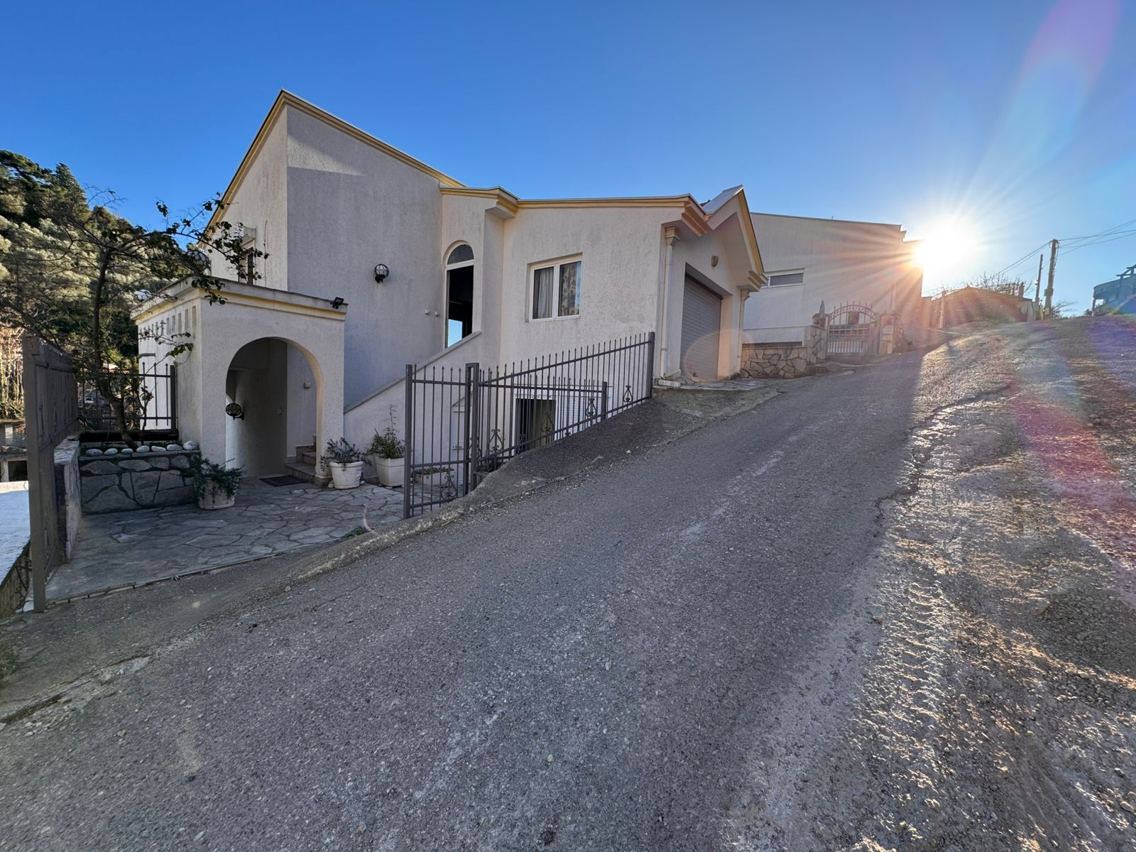 Elegant two-story white house in Ulcinj, Montenegro with arched entryway, metal gate, and hill views&mdash;exclusive at immobilien.ekosphere.me.
