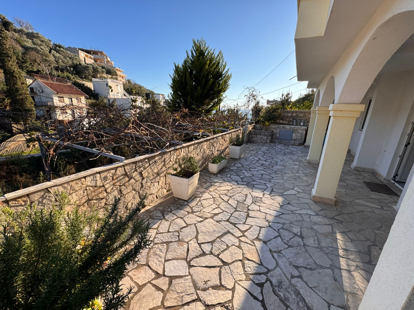 Elegant stone terrace with potted plants, arches, and scenic Ulcinj views. Prime investment via immobilien.ekosphere.me by ekosphere doo.