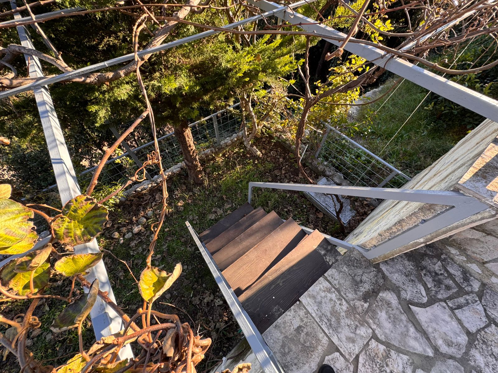 Elegant outdoor wooden stairs with sleek metal railings, lush greenery, and secure fencing&mdash;prime Ulcinj investment via immobilien.ekosphere.me by ekosphere doo.