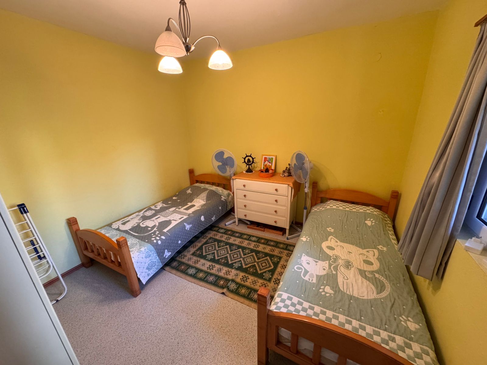 Cozy Ulcinj bedroom with vibrant yellow walls, twin wooden beds, green rug, and ample storage&mdash;a great Montenegro investment.