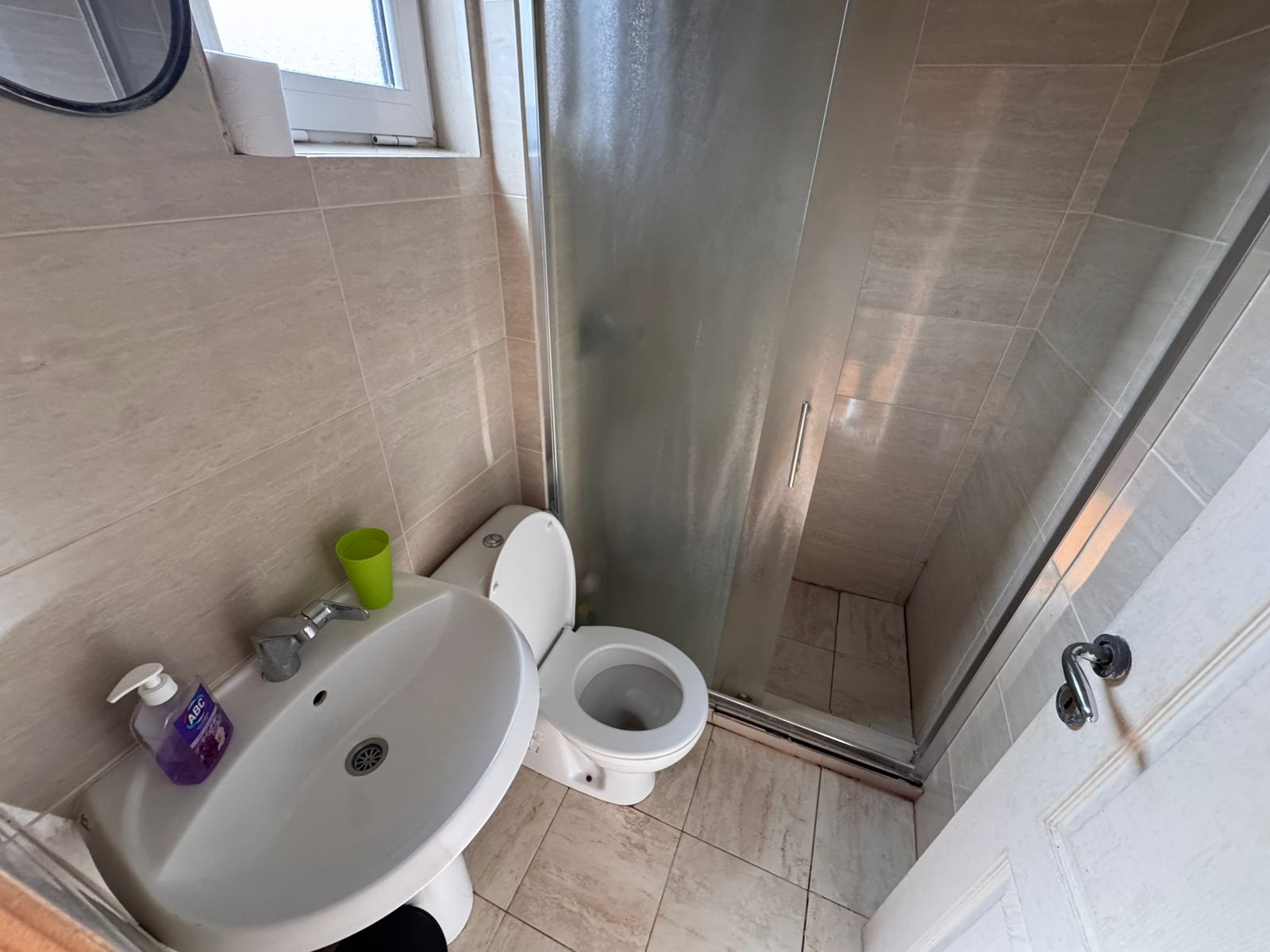 Modern Ulcinj bathroom with beige tiles, glass shower, window, and stylish fixtures&mdash;prime property via immobilien.ekosphere.me by ekosphere doo.