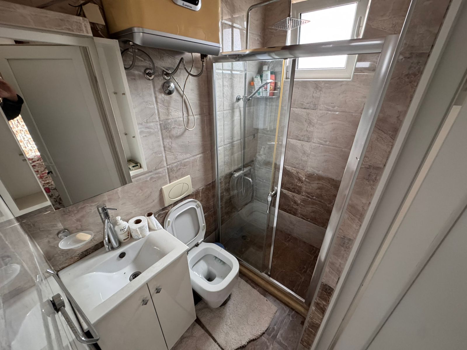 Modern bathroom in Ulcinj with beige tiles, glass shower, bright window, and quality fixtures. Exclusive at immobilien.ekosphere.me.