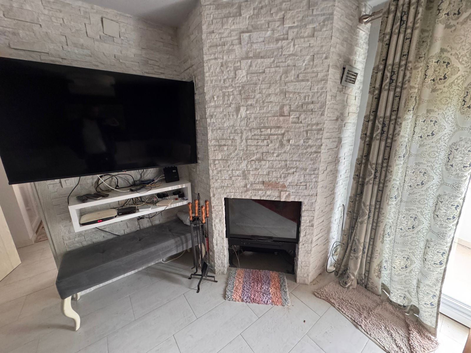 Modern Ulcinj living room with wall-mounted TV, fireplace, and stylish accents&mdash;ideal Montenegro real estate at immobilien.ekosphere.me.