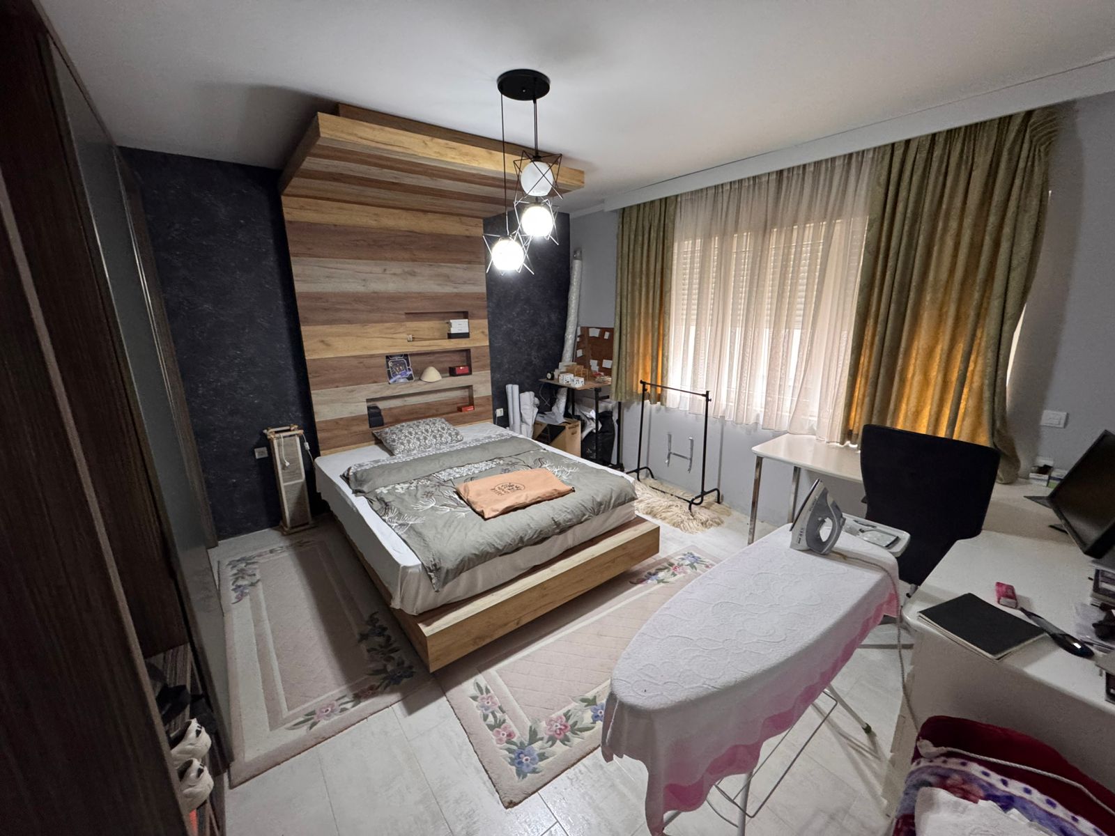 Stylish Ulcinj bedroom with wooden bed, modern lighting, desk, large green-curtained windows. Exclusive on immobilien.ekosphere.me by ekosphere doo.