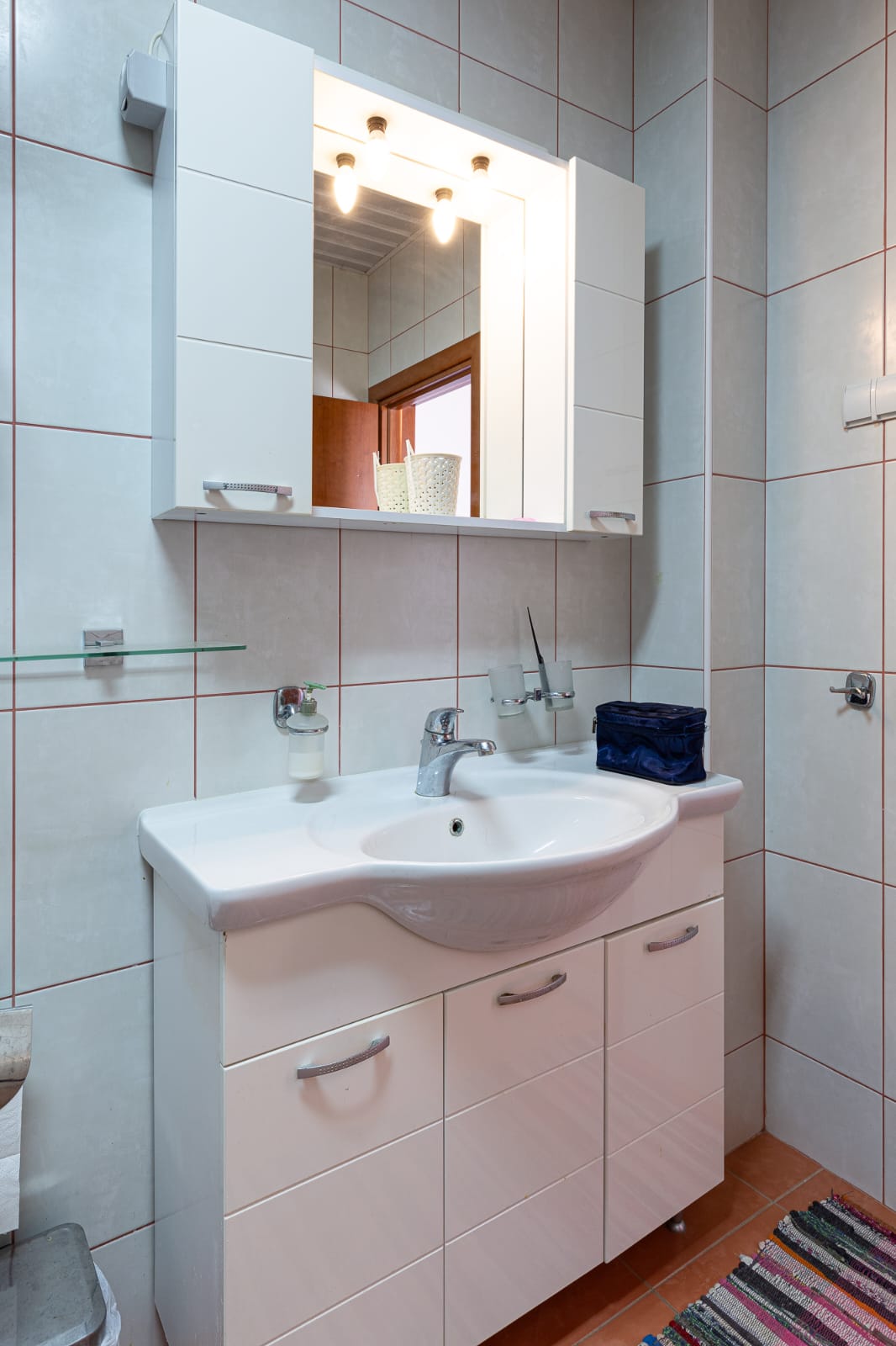 Modern Ulcinj bathroom: white tiles, sleek sink cabinet, illuminated mirror. Perfect for property investment at immobilien.ekosphere.me.