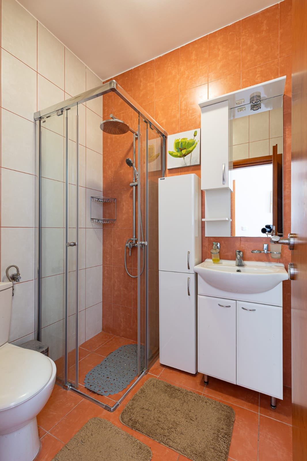 Modern Ulcinj bathroom with stylish orange-white tiles, glass shower, premium fixtures. Exclusive on immobilien.ekosphere.me by ekosphere doo.
