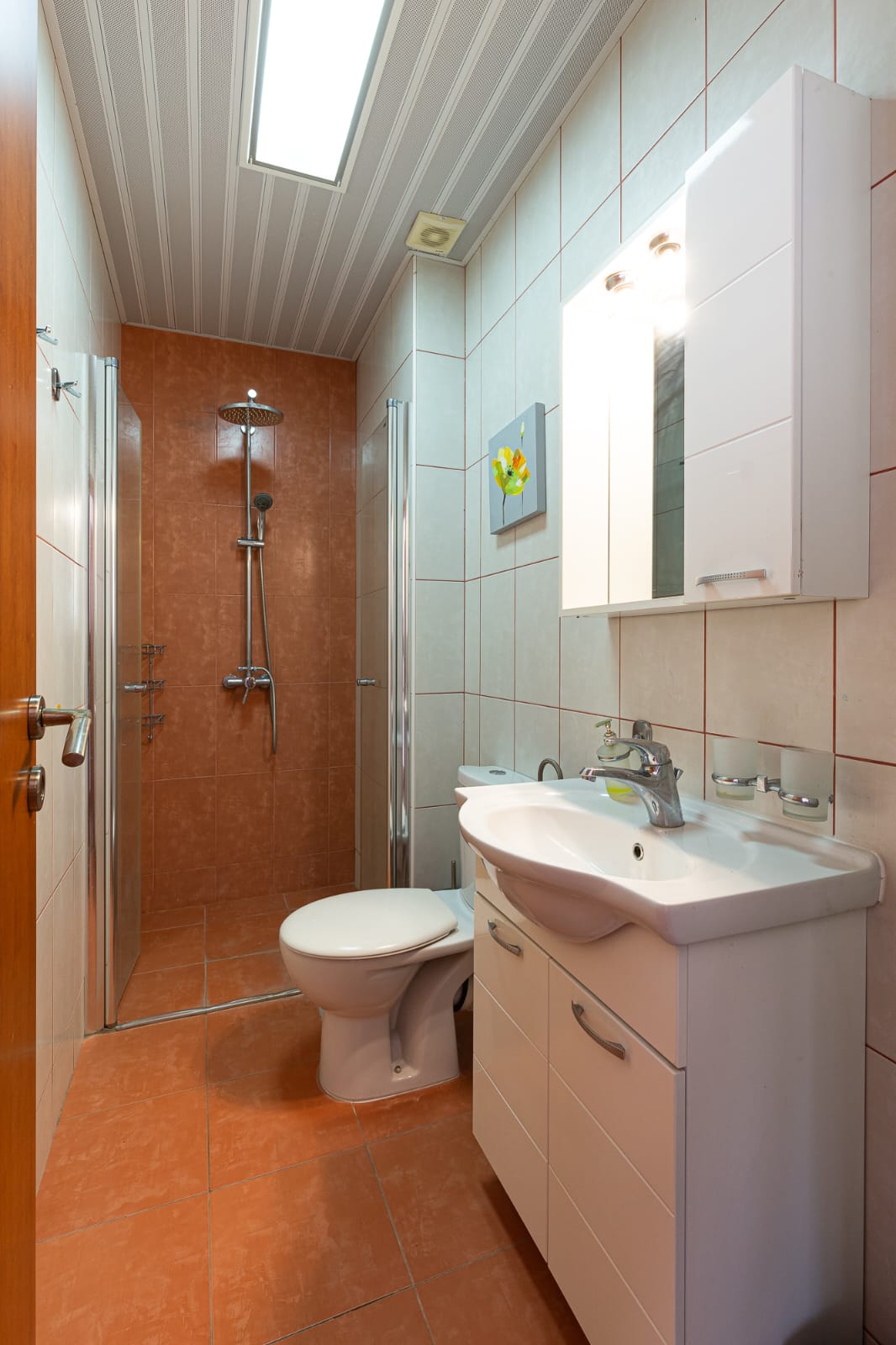 Modern, space-efficient bathroom in Ulcinj with orange tiles, premium fixtures, glass shower. Invest via immobilien.ekosphere.me by ekosphere doo.