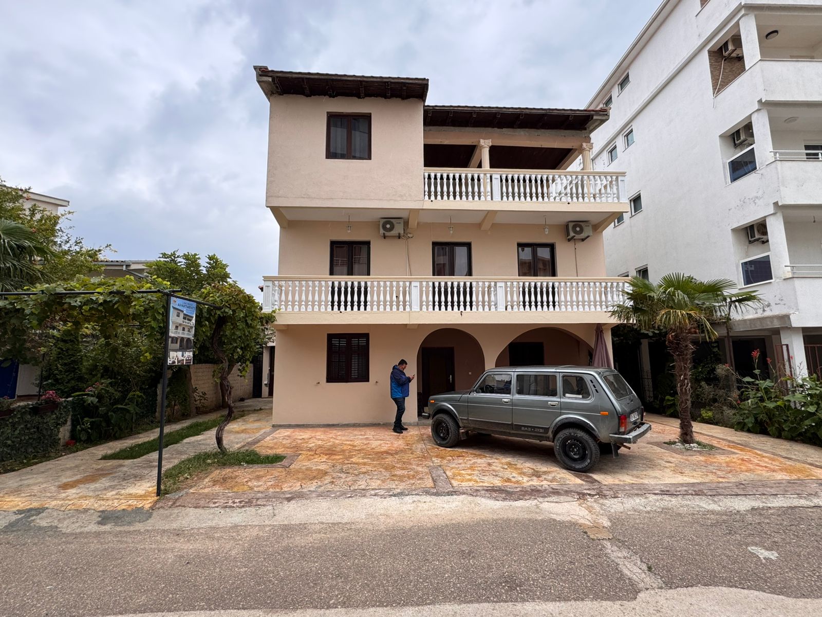 Modern three-story beige residence with balconies, tiled roof, and palm&mdash;prime Ulcinj investment via immobilien.ekosphere.me by ekosphere doo.