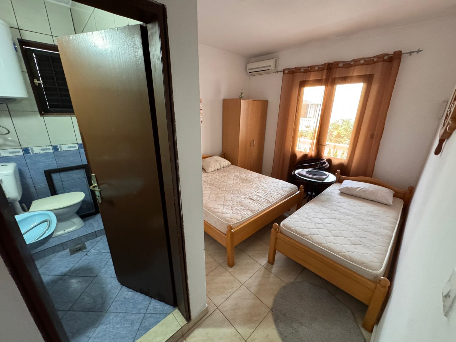 Bright Ulcinj bedroom with twin beds, wardrobe, window, and modern tiled bathroom&mdash;an ideal investment via immobilien.ekosphere.me.