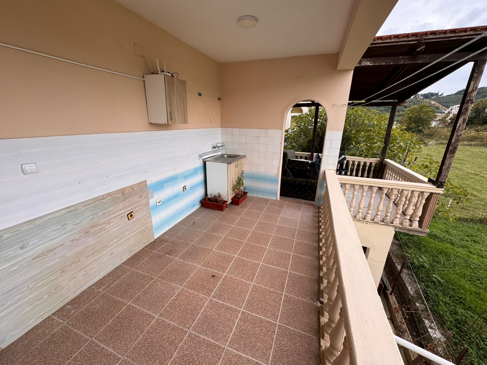 Spacious tiled balcony in Ulcinj with sink, covered seating, and peaceful green views&mdash;ideal Montenegro investment at immobilien.ekosphere.me.