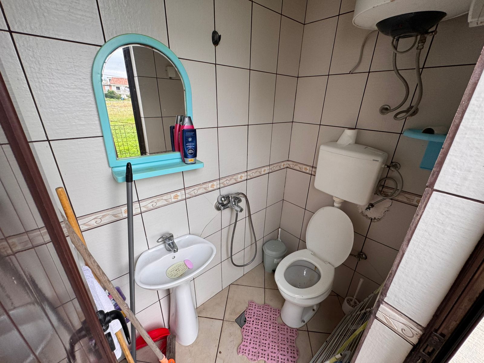 Modern tiled bathroom featuring a sink, mirror, and toilet, water heater, pink mat; ideal Ulcinj investment via immobilien.ekosphere.me.