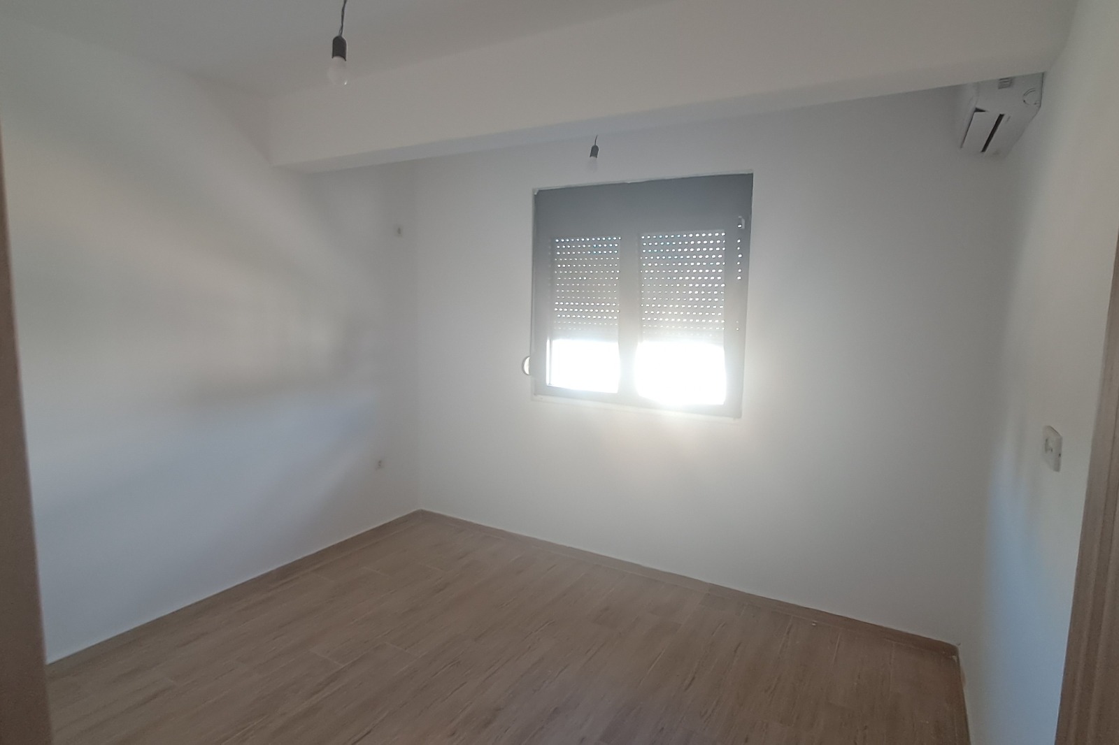 Bright, modern Ulcinj apartment with white walls, wood flooring, AC unit; sunlight through window. Invest via immobilien.ekosphere.me by ekosphere doo.